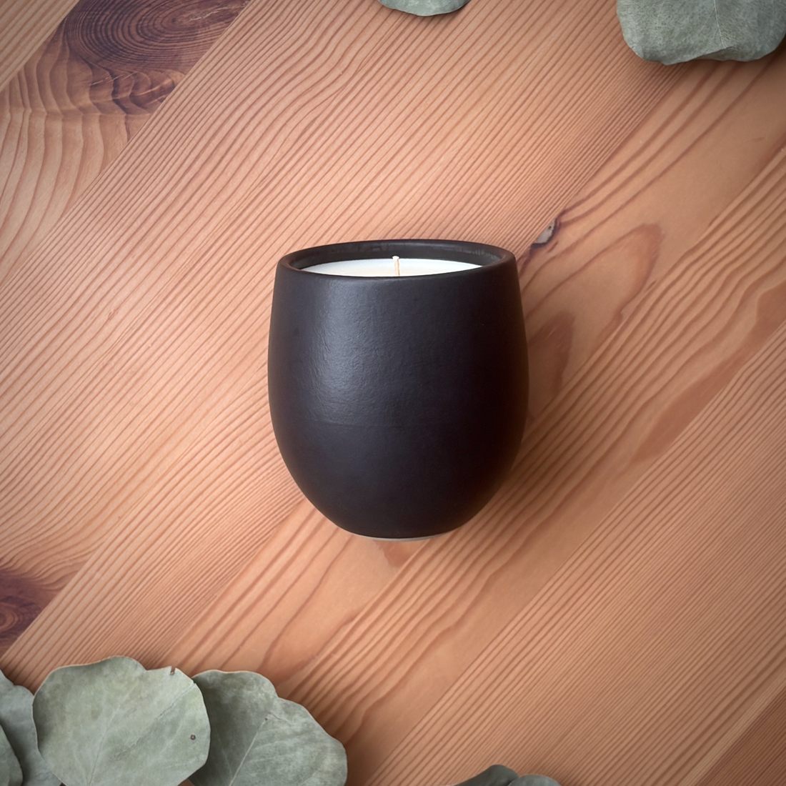 A matte black organic candle on a wooden surface