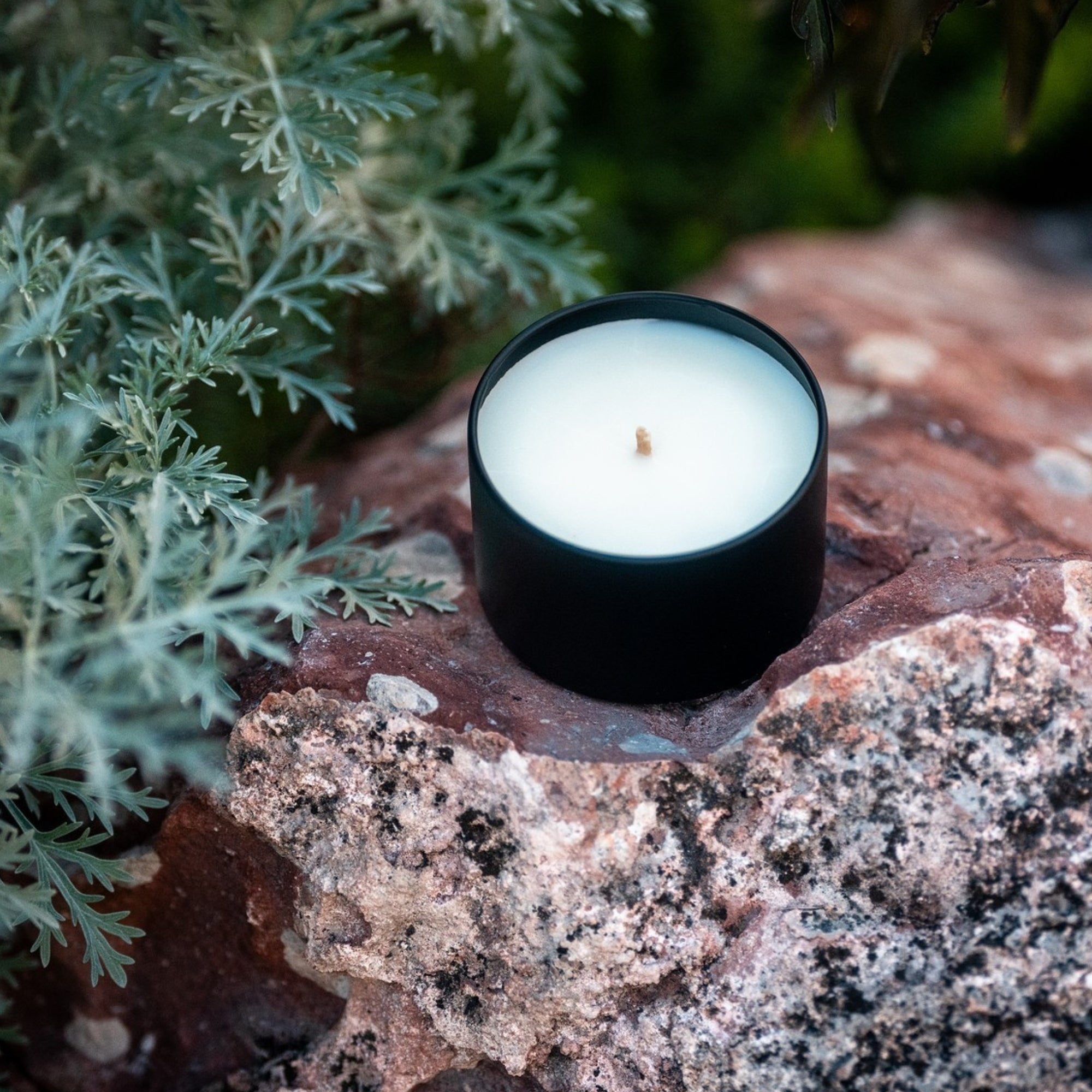 Black organic candle on a rock with greenery